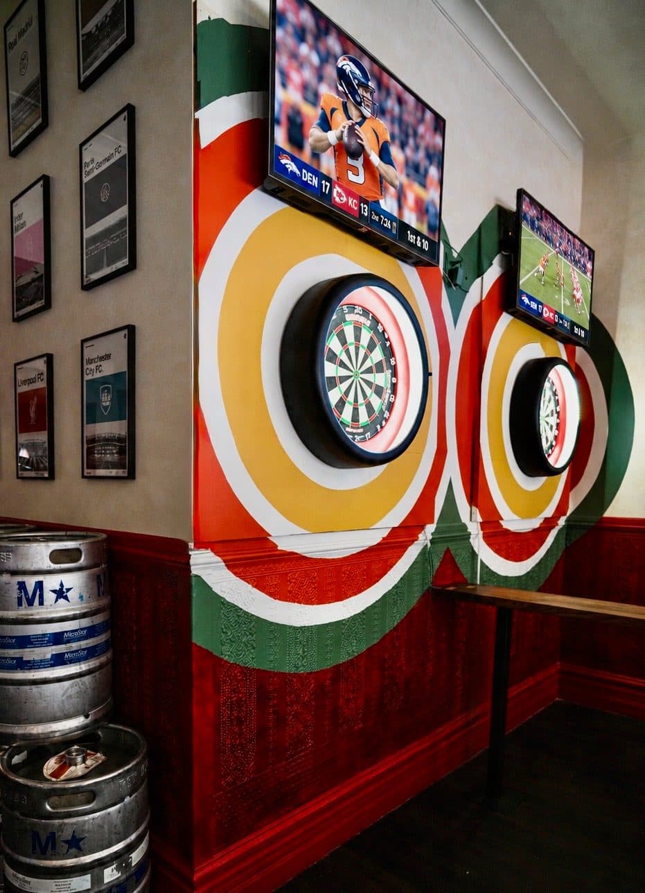 Two lit darts boards in painted rings, with the game on the screens above, at BARna