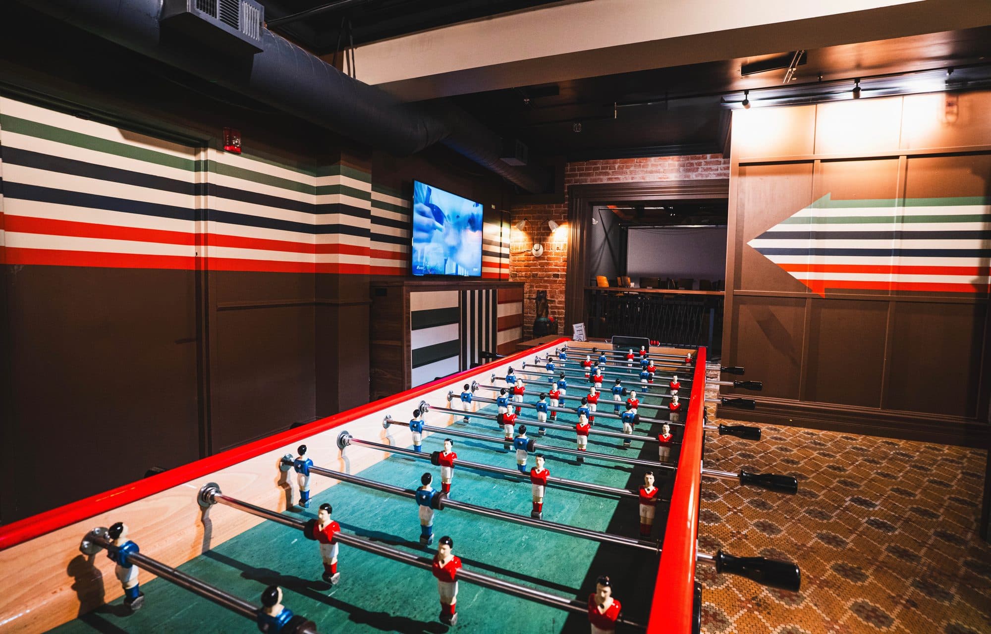 A full size foosball table in front of the striped walls on the lower level at BARna