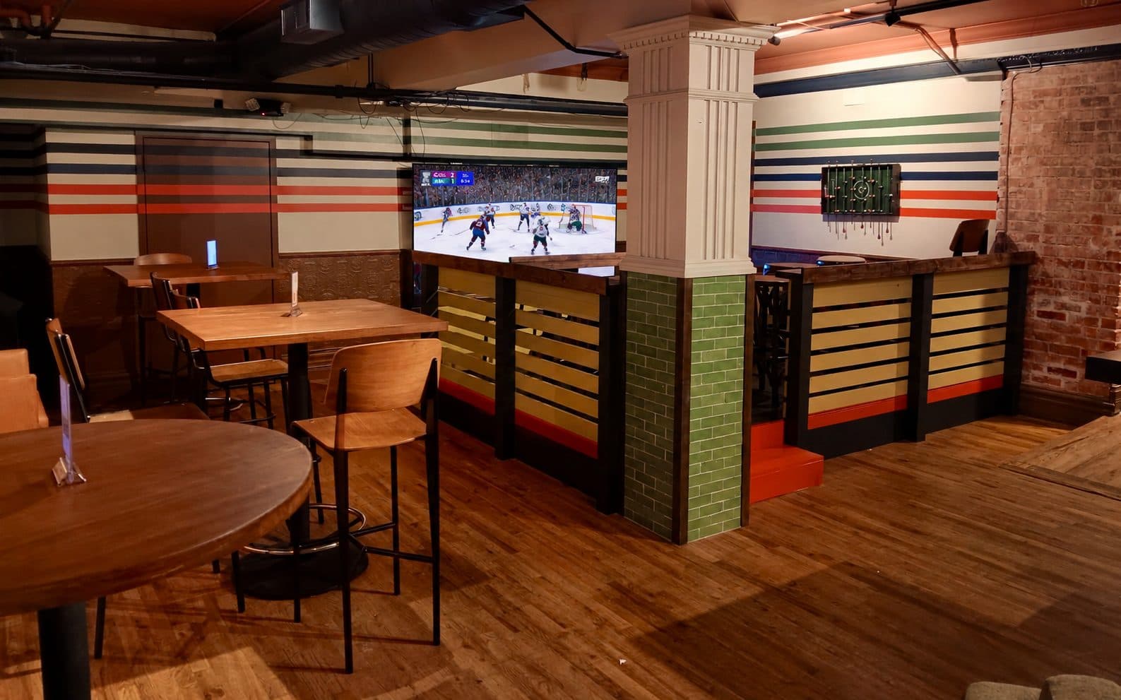 Tables, a green tiled pillar and a game on the big screen on the lower level at BARna