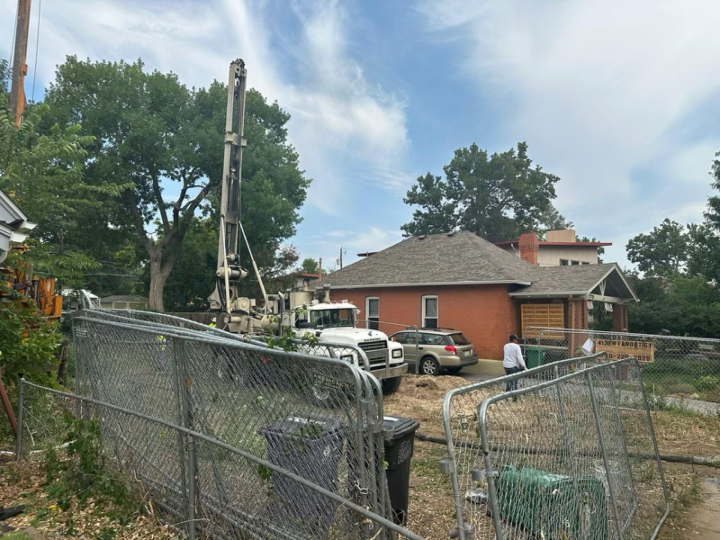 Drilled-pier rig on a fenced Denver jobsite next to the existing brick home